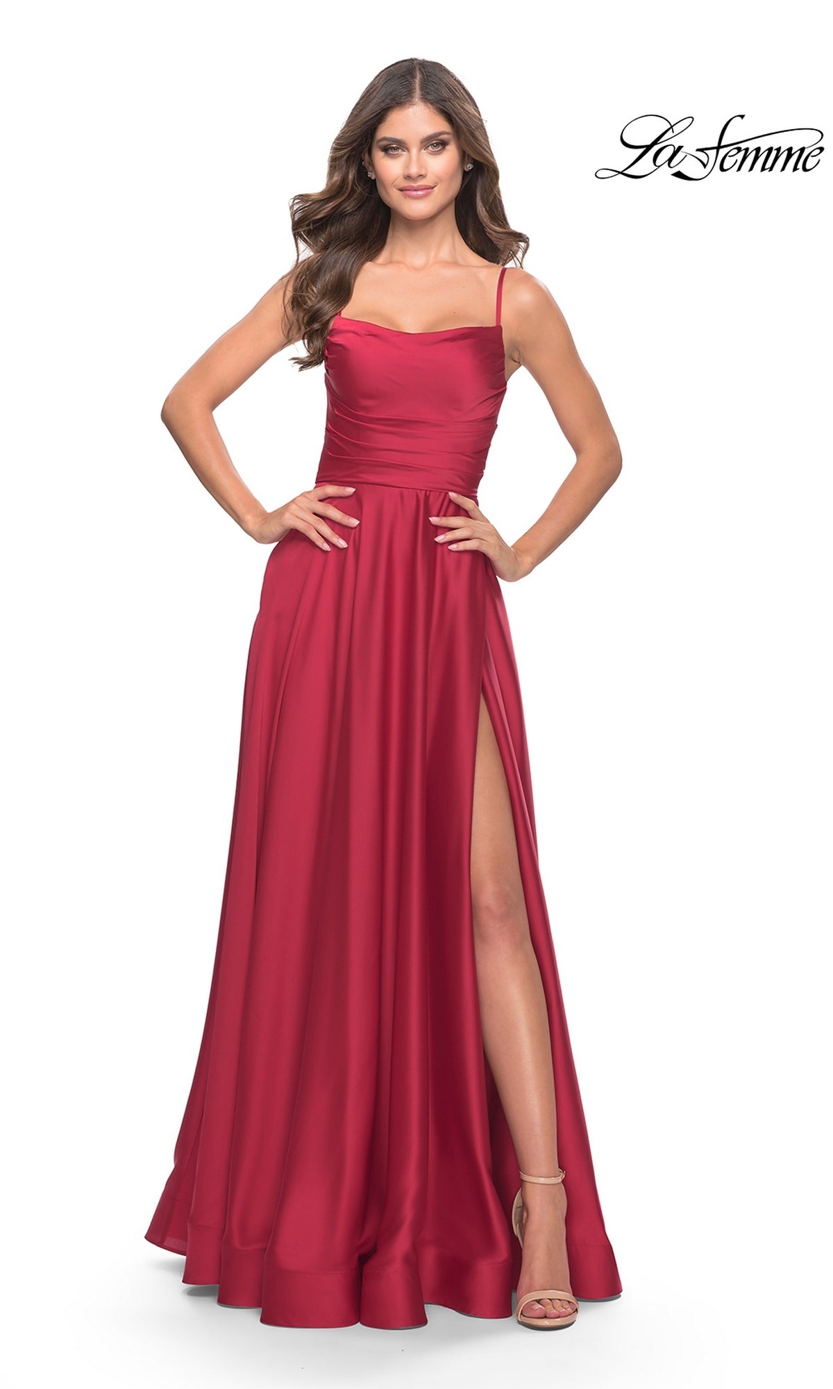 A woman poses in the Corset-Back La Femme Long A-Line Prom Dress 31105, a sleeveless, floor-length red satin gown with thin straps, a high slit, and corset back. She wears nude heels. The La Femme logo appears in the top right corner.